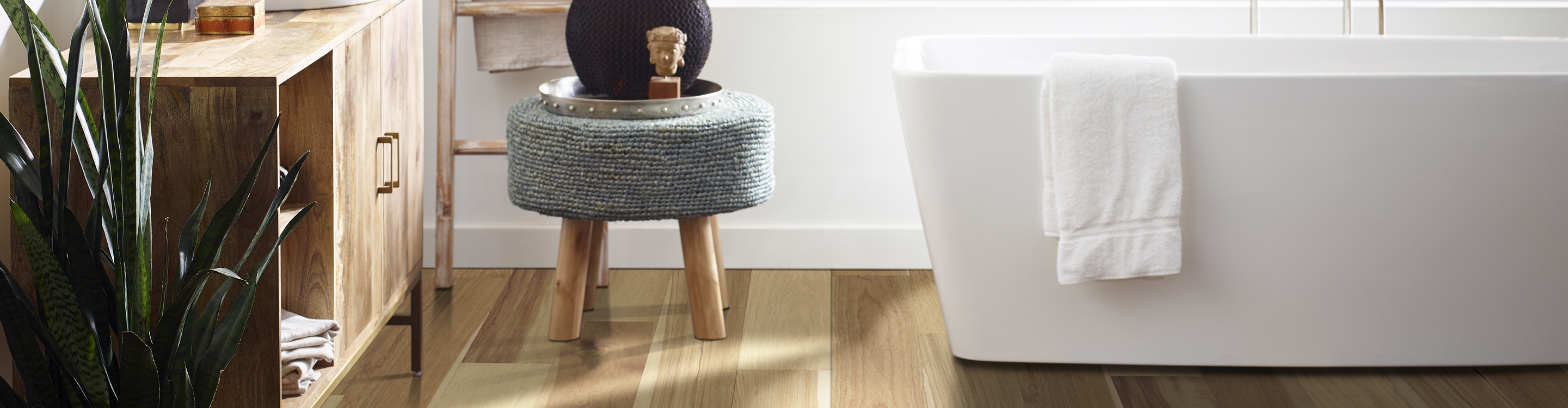 Light wood floors in bathroom with white soaker tube and gray stool